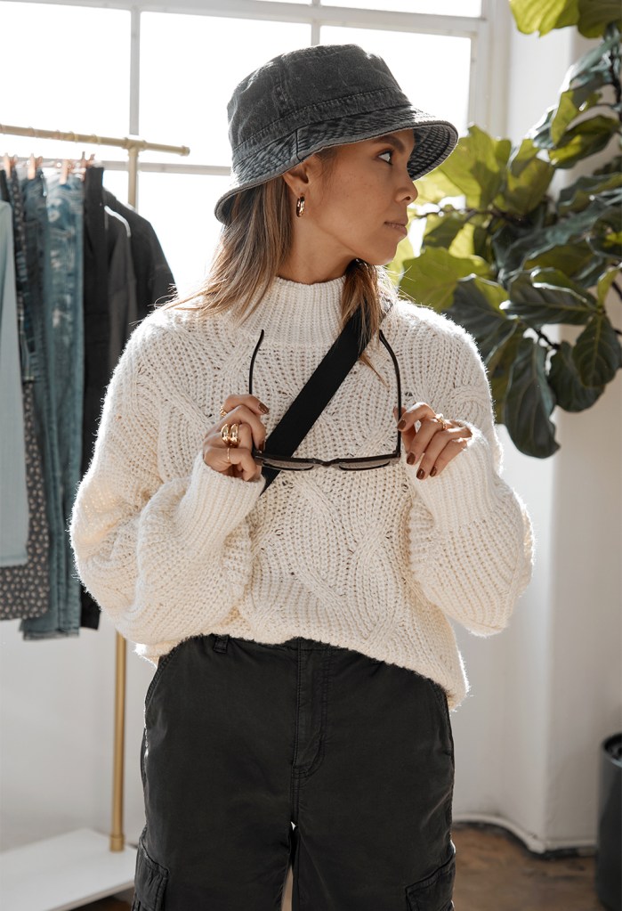 woman wearing a cream color sweater, black pants, and a bucket hat