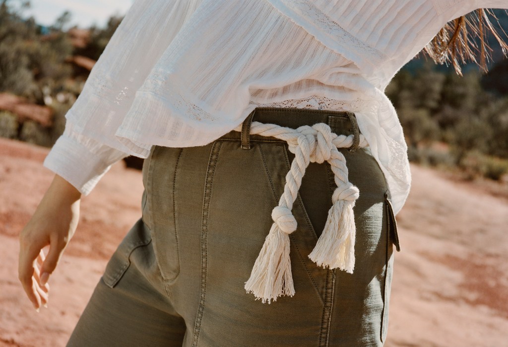 close up image of a woman wearing green pants with a braided belt and a white top