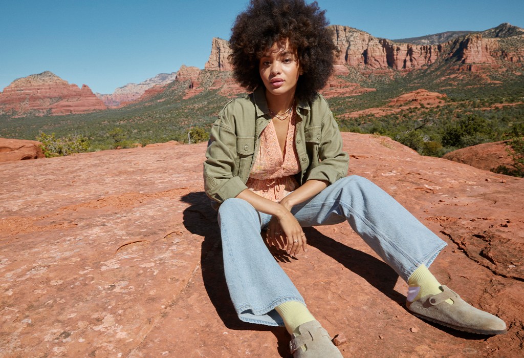 woman wearing light wash '90s wide leg jeans, an orange shirt, and a green shacket