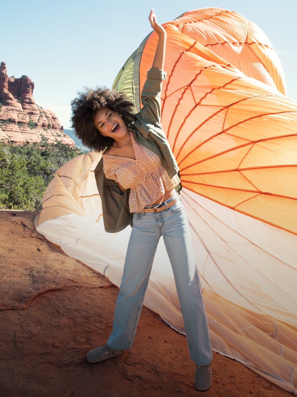 woman wearing light wash '90s jeans, an orange shirt, and a green jacket