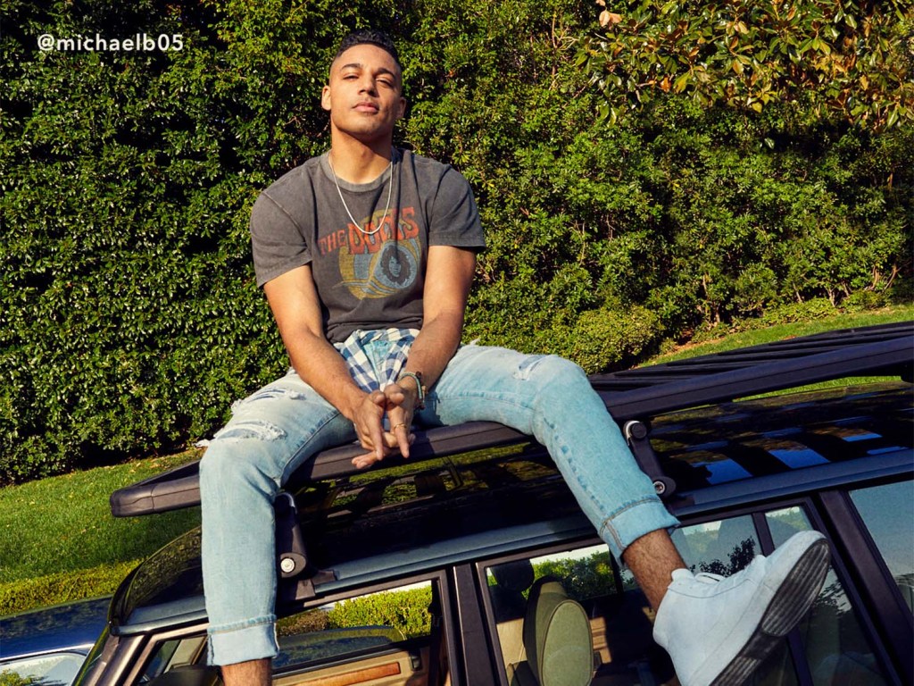 guy wearing a graphic tee and American Eagle light wash jeans sitting on top of a car