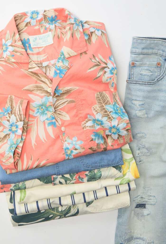 a stack of printed Hawaiian shirts next to light wash ripped jeans from American Eagle