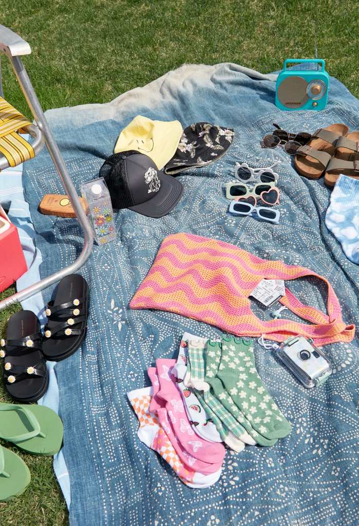 a blue blanket in grass with sunglasses, bags, sandals, and hats from American Eagle on top