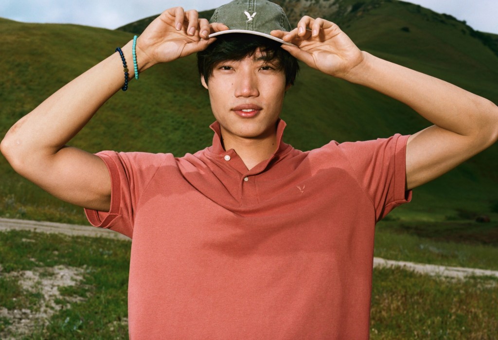 guy wearing a red American Eagle polo shirt and a green baseball hat in front of a mountain scenery