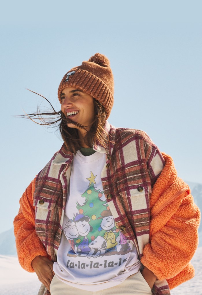 girl with brown hair wearing a brown beanie hat, orange sherpa jacket, plaid shacket, and Peanuts graphic tee from American Eagle