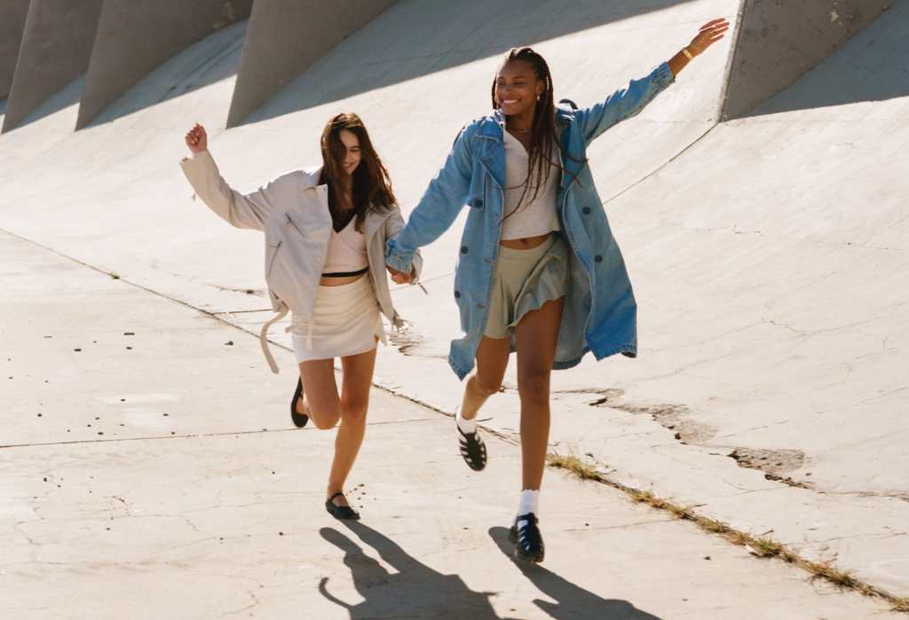 two girls wearing american eagle skirts, crop tops, and overshirts running on a street