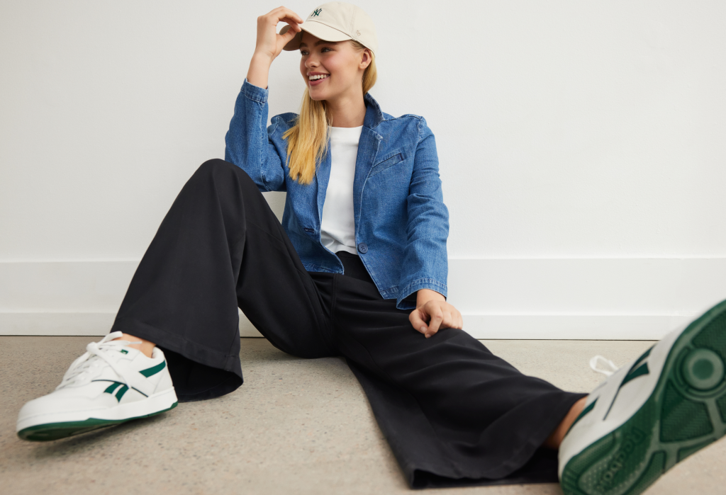 girl wearing a white baseball hat, white tshirt, denim jacket, and black trousers from American Eagle