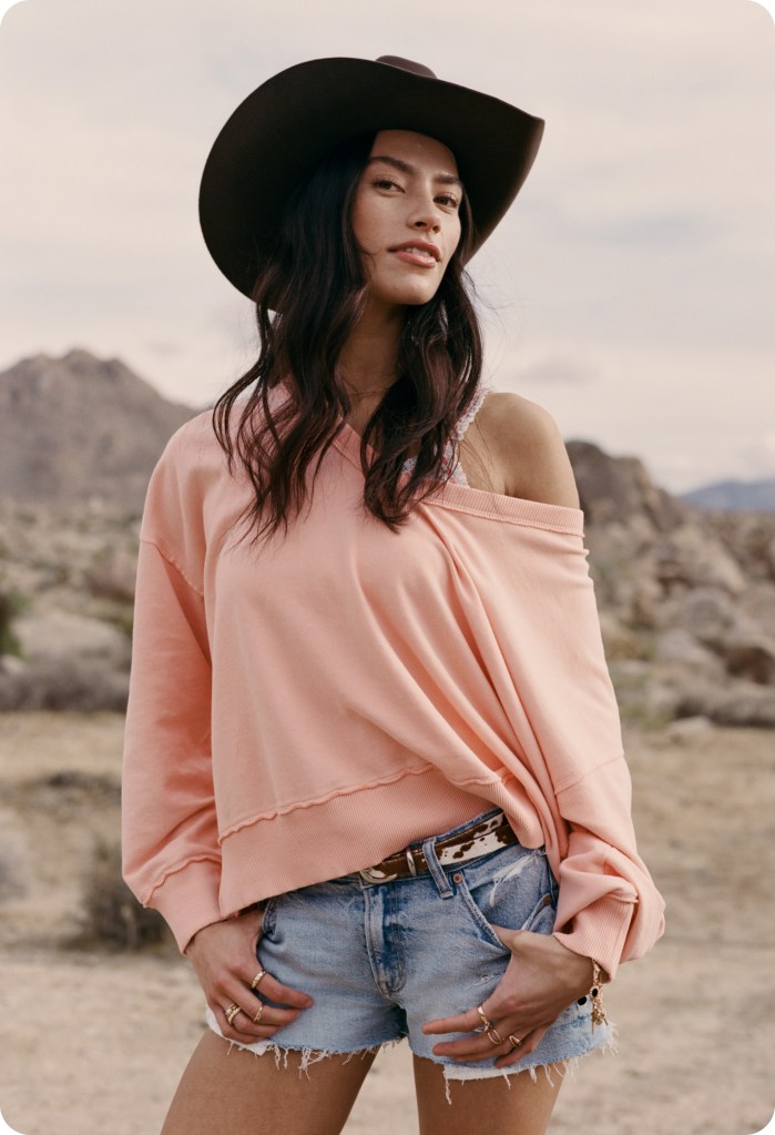 girl wearing a country festival outfit of oversized top, jorts, and cowboy hat from american eagle